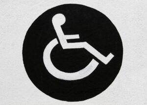 na czarnym kółku na biało osoba siedząca na wózku inwalidzkim